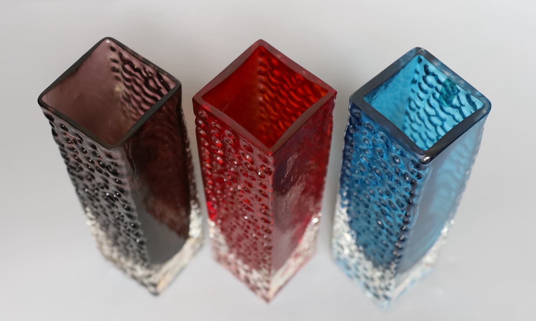 A trio of Whitefriars 'Nailhead' vases, designed by Geoffrey Baxter, kingfisher blue, red and amethyst glass, 20 cms high